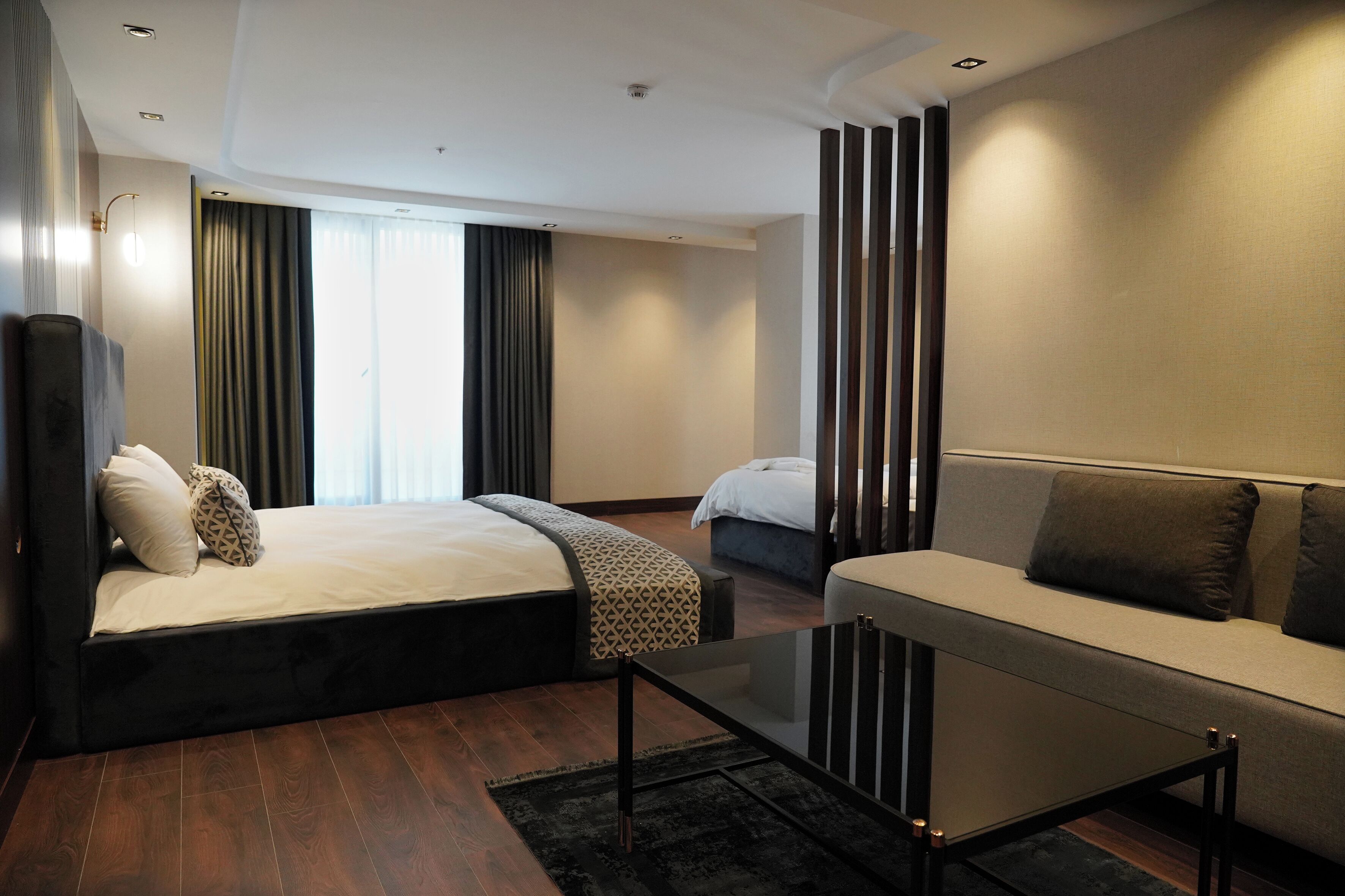 A modern hotel room with a bed, sofa, and a glass coffee table.