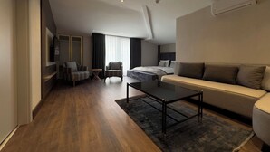 A modern hotel room with a wooden floor, a sofa, a coffee table, a TV, a chair, and a bed. - Nevizade Avangart Hotel (Istanbul)