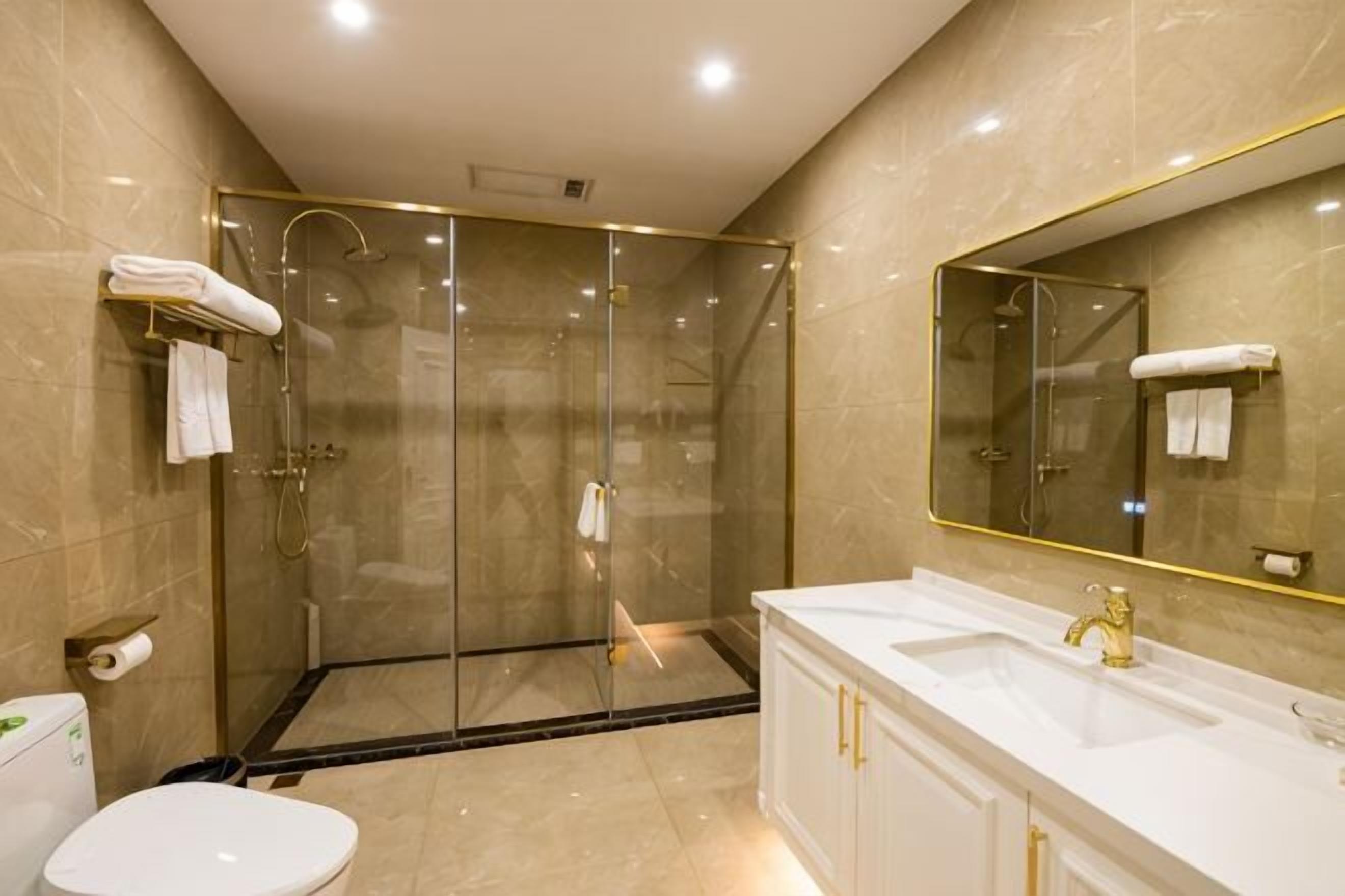 A modern bathroom with a glass-enclosed shower, a white sink with gold fixtures, and a large mirror.