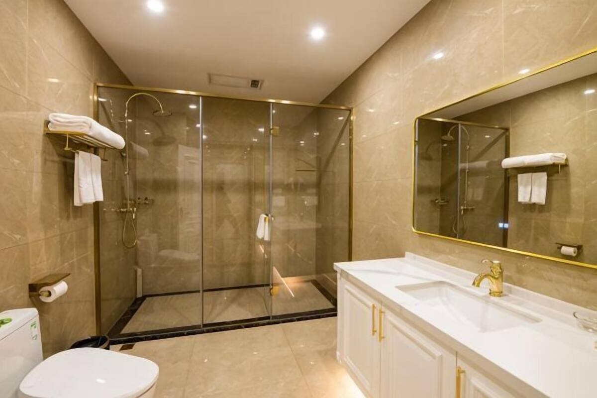 A modern bathroom with a glass-enclosed shower, a white sink with gold fixtures, and a large mirror.