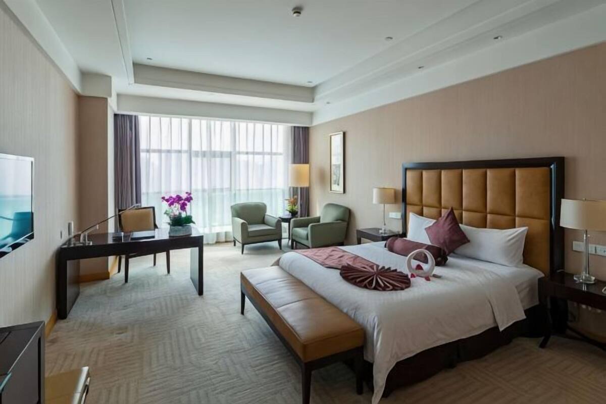 A hotel room with a large bed, a desk, two chairs, a television, and a window with curtains.