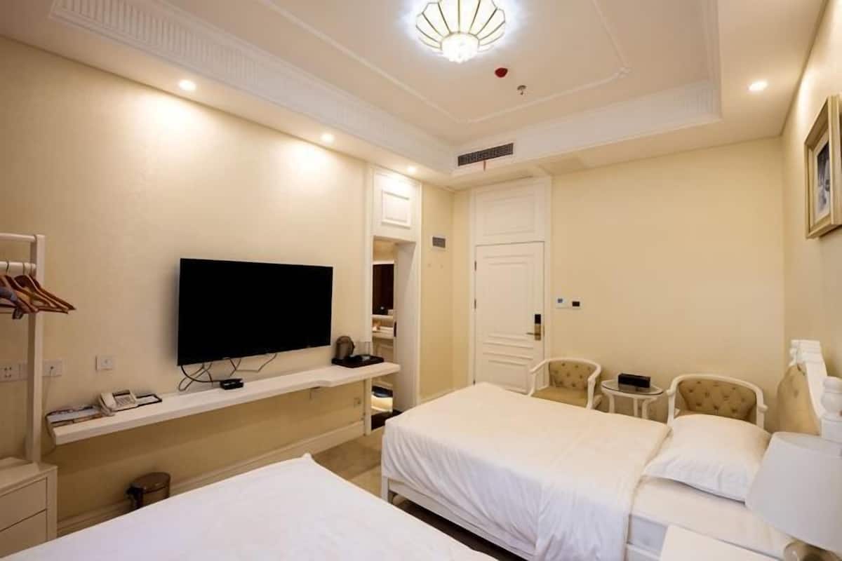 A hotel room with two beds, a TV, a mirror, a chair, and a small table.