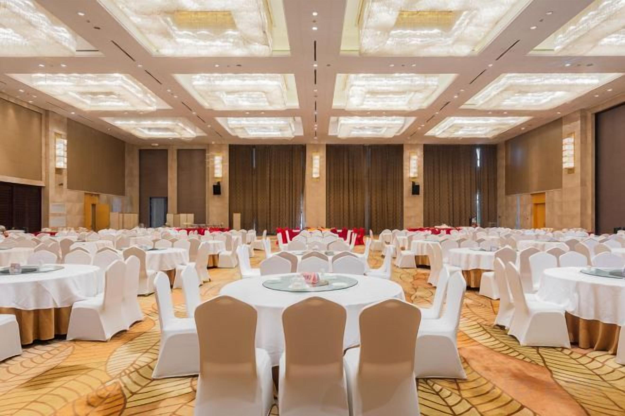 A banquet hall with round tables and chairs, a carpeted floor, and a high ceiling with recessed lighting.