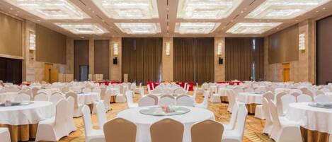 A banquet hall with round tables and chairs, a carpeted floor, and a high ceiling with recessed lighting.