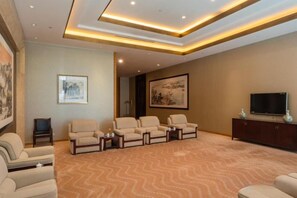 A spacious living room with a large flat-screen TV, multiple seating options, and a patterned carpet. - Grand Shaanxi Hotel (Xi'an)