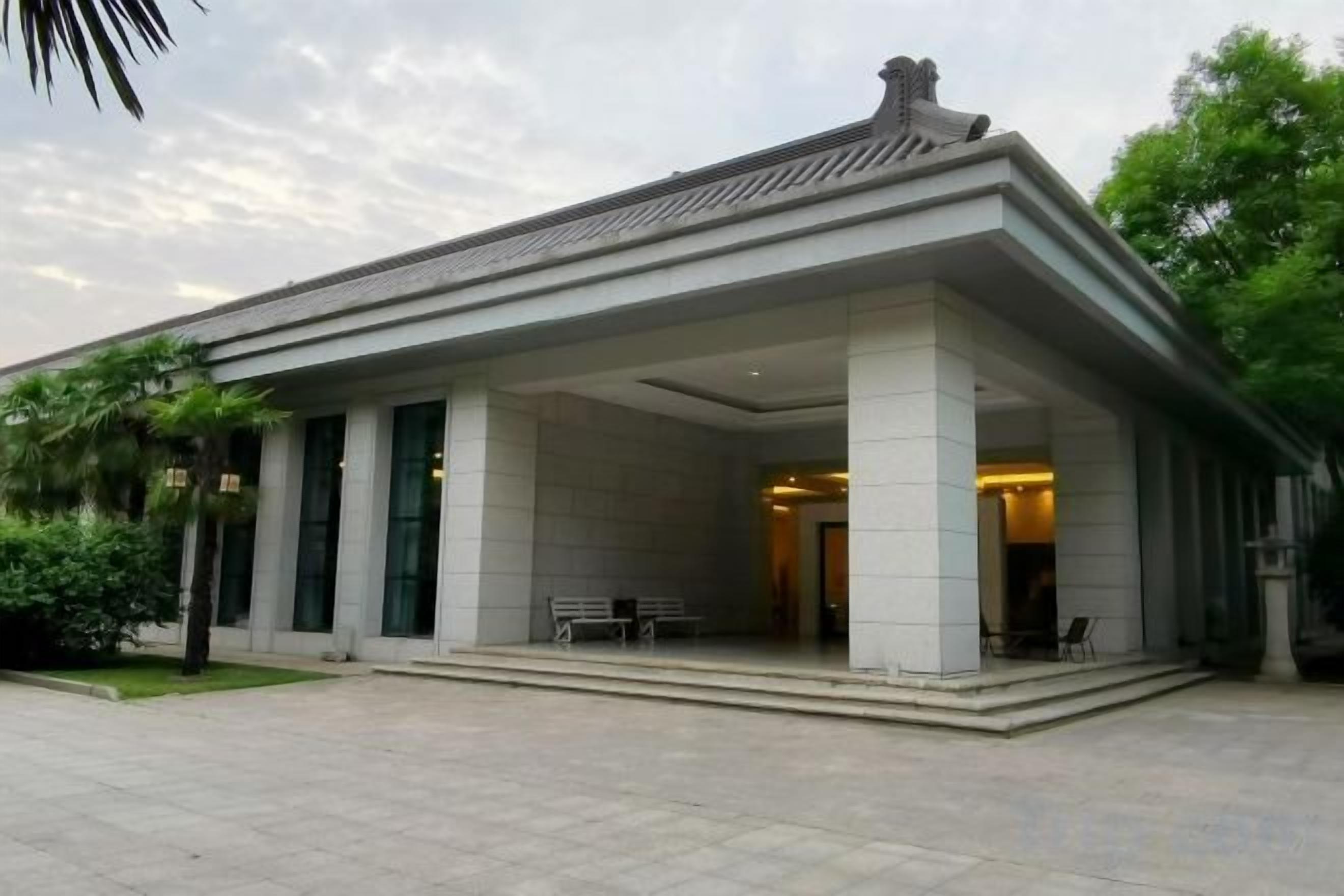 A building with a covered entrance, columns, and a paved area.