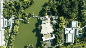An aerial view of a building complex with a central courtyard, surrounded by dense greenery and a body of water.