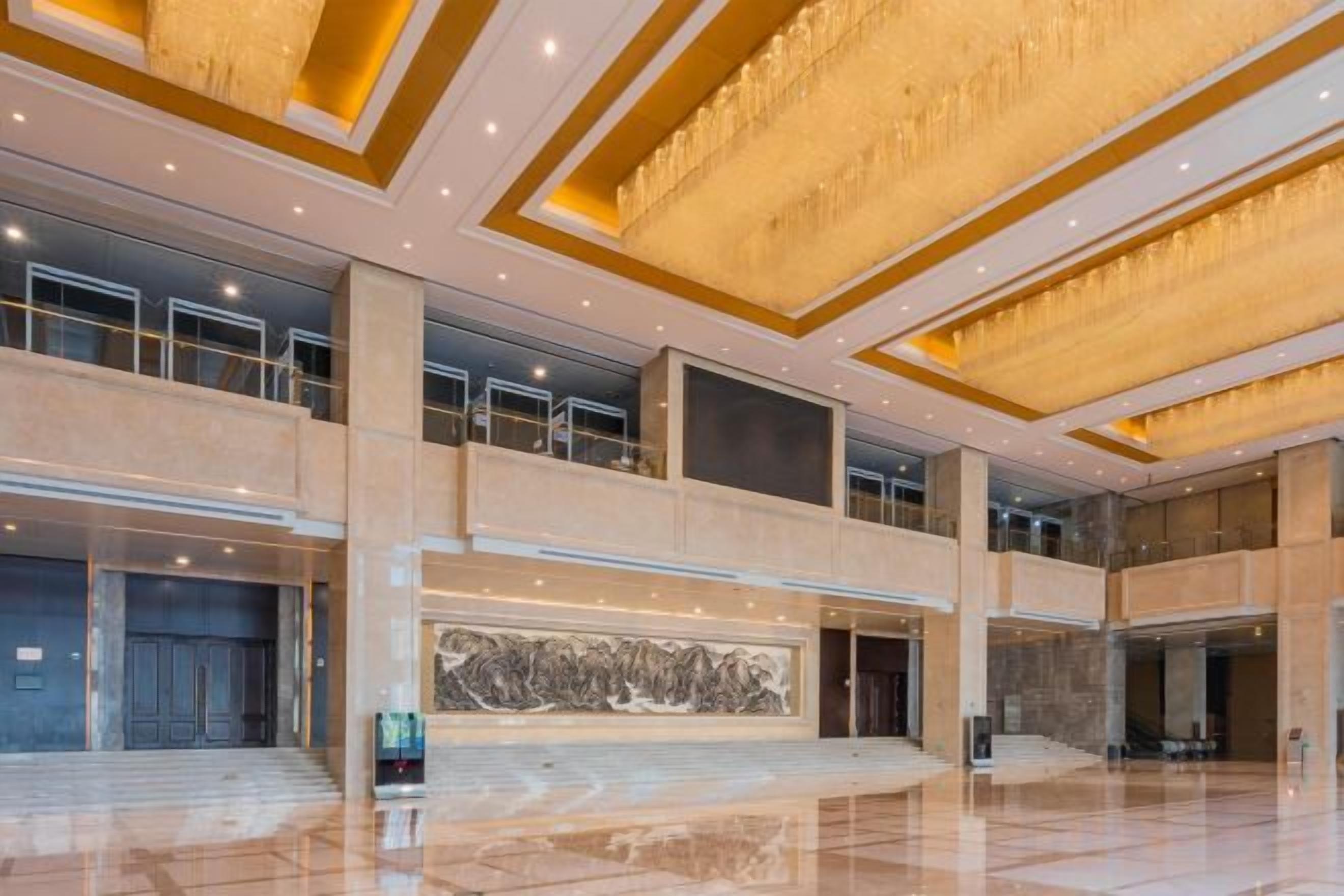A spacious lobby with a high ceiling, large windows, and a grand staircase.