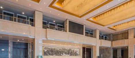 A spacious lobby with a high ceiling, large windows, and a grand staircase.