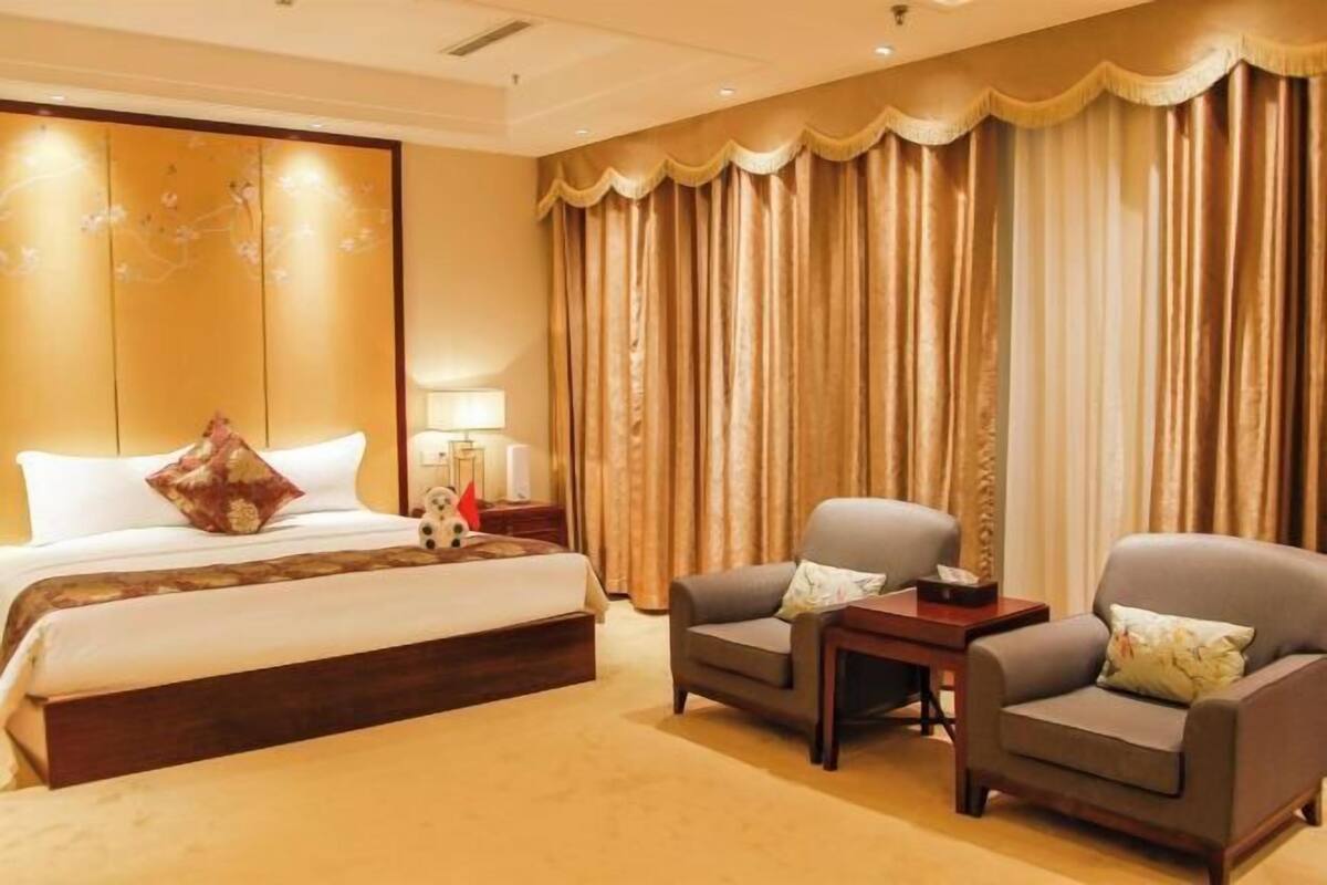A hotel room with a large bed, two armchairs, a small table, and a curtain.