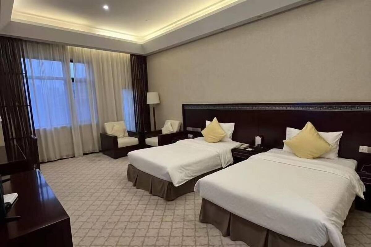 A hotel room with two beds, a desk, a chair, and a window with curtains.