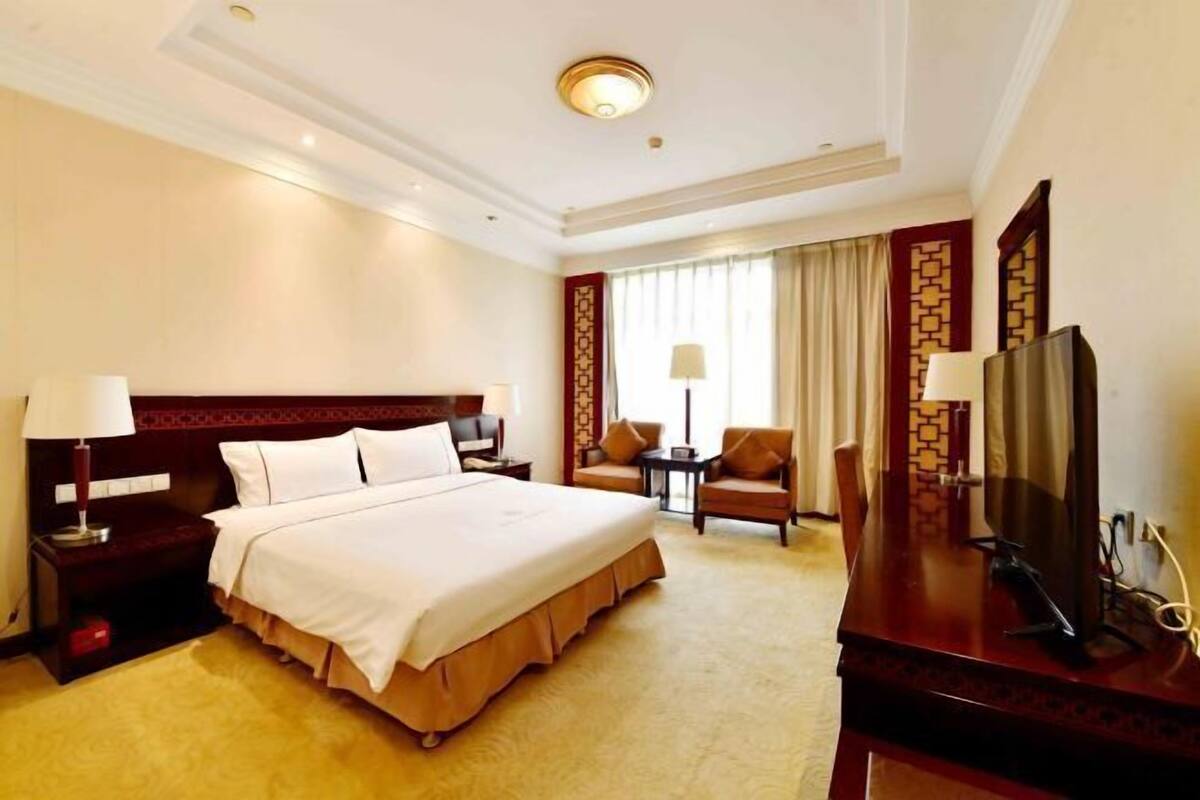 A hotel room with a large bed, a desk, a chair, a TV, and a window with curtains.