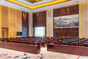 Une salle de conférence avec des rangées de chaises, une longue table et un grand tableau accroché au mur.