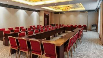 A conference room with a long table and red chairs, a patterned carpet, and a modern ceiling design.