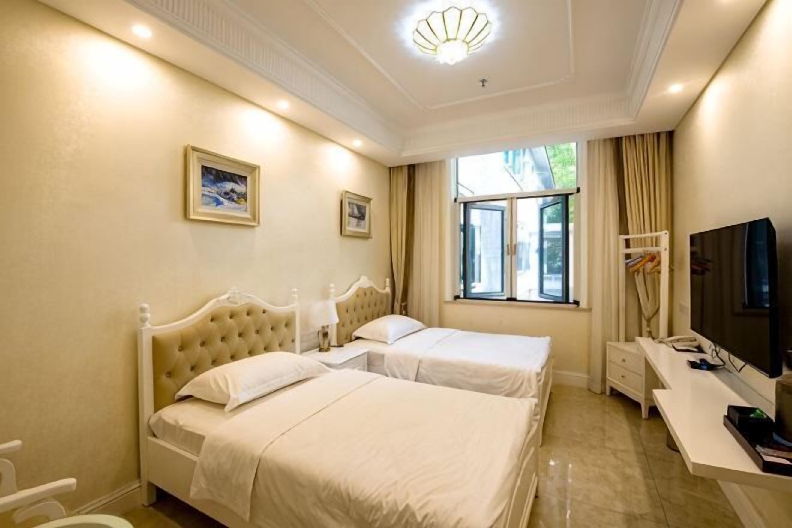 A hotel room with two beds, a desk, a TV, and a window with curtains.