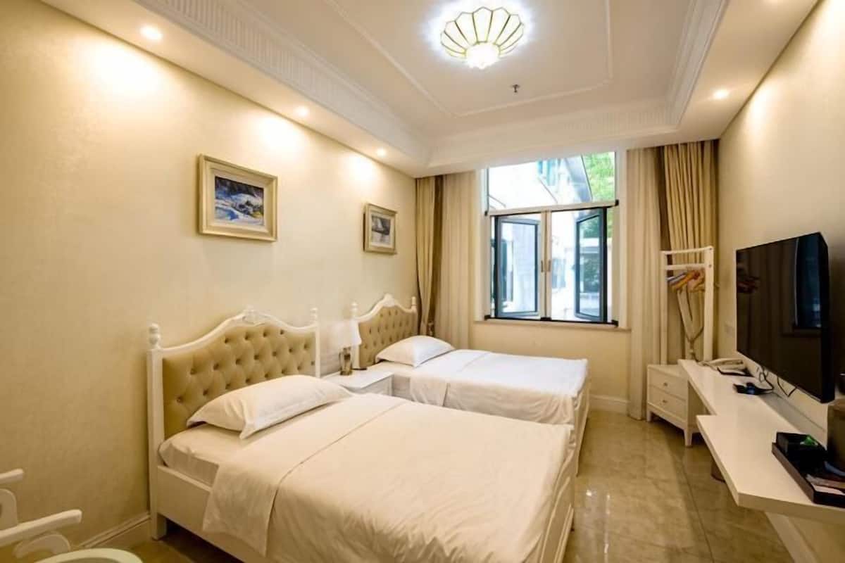 A hotel room with two beds, a desk, a TV, and a window with curtains.