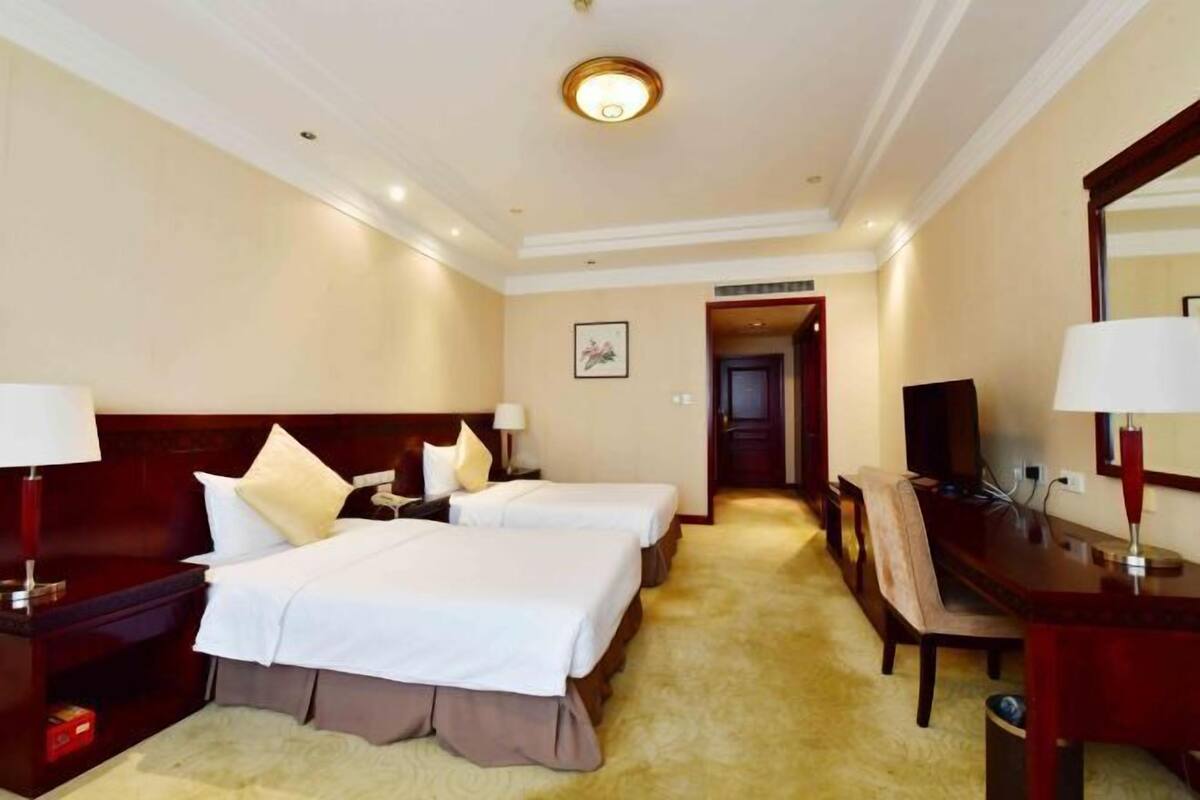 A hotel room with two beds, a desk, a chair, a TV, and a mirror.