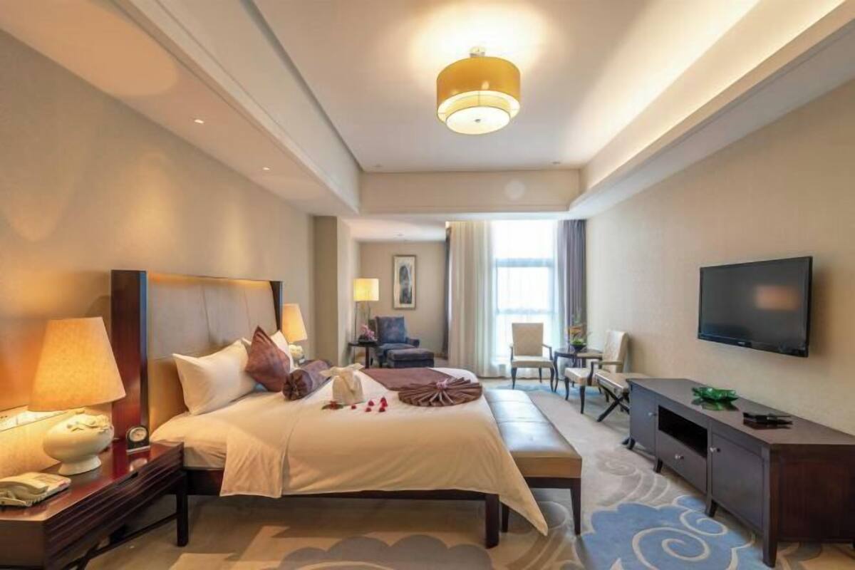 A hotel room with a bed, bedside tables, a TV, a desk, and a chair.