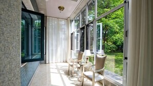 Una habitación iluminada por el sol con ventanas amplias, una zona de estar con sillas y una mesa, y vistas a la vegetación.