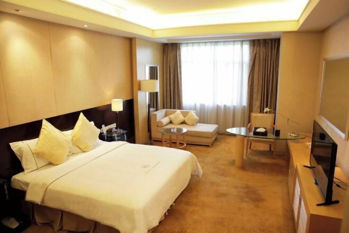 A hotel room with a large bed, a sofa, a small table, a TV, and a window with curtains.