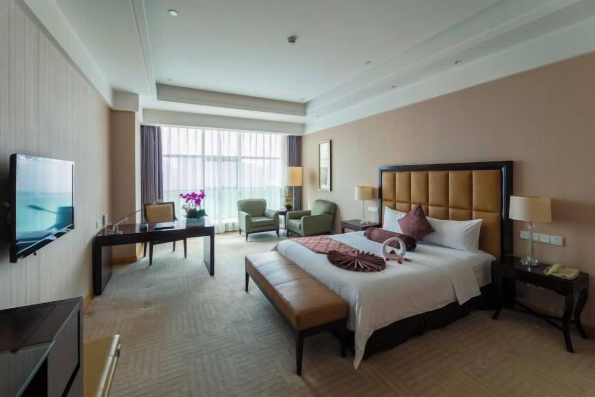 A hotel room with a large bed, a desk, a TV, and a window with curtains.