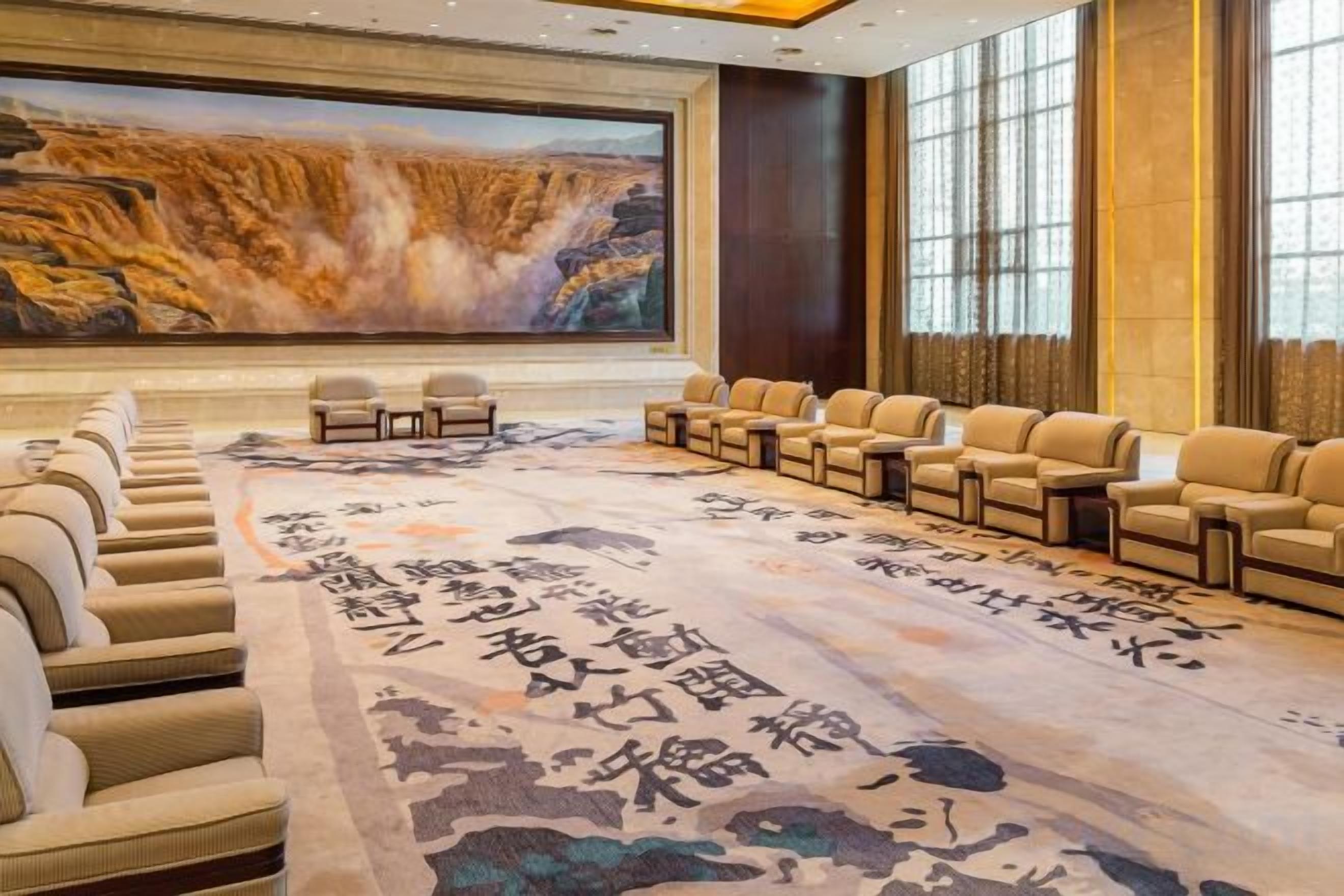 A conference room with a large screen, rows of chairs, and a carpet with calligraphy.