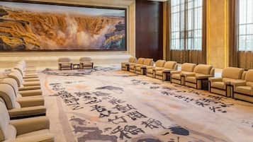 A conference room with a large screen, rows of chairs, and a carpet with calligraphy.