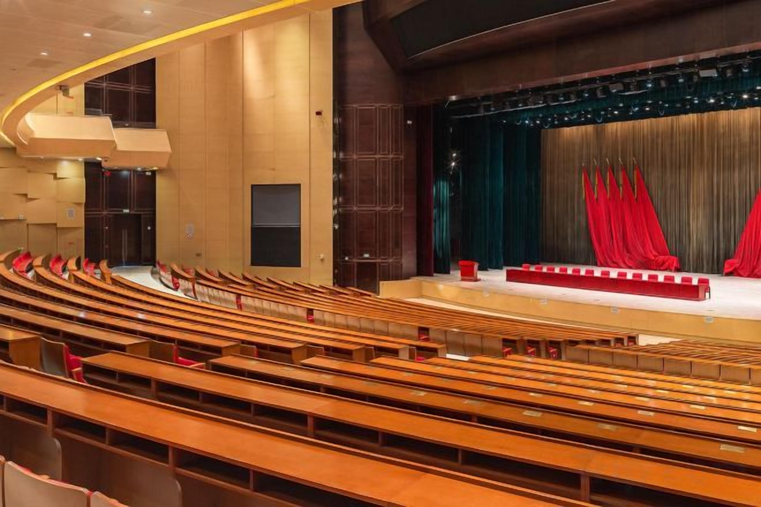 An auditorium with tiered seating and a stage with red curtains.
