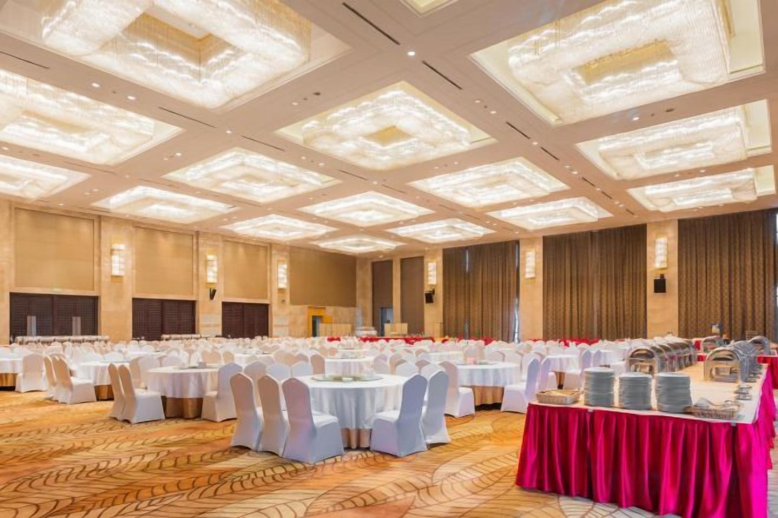 A banquet hall with round tables, white chairs, and a red tablecloth.