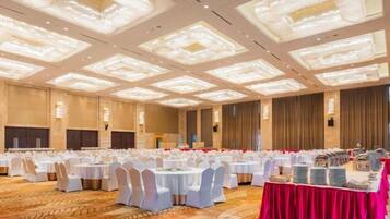 A banquet hall with round tables, white chairs, and a red tablecloth.