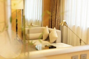 Un salon moderne avec un canapé, des coussins, une lampe et une vue sur l’extérieur à travers une fenêtre ornée de rideaux.