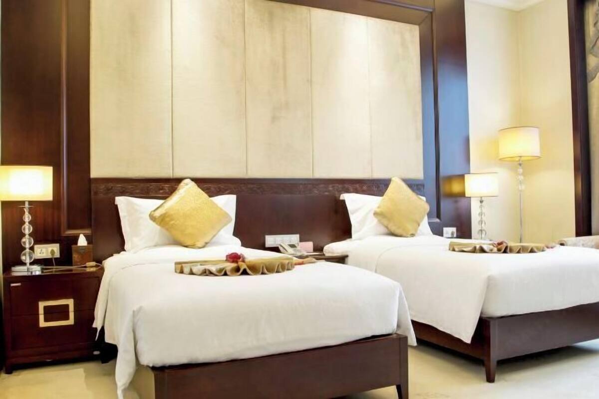 A hotel room with two beds, wooden headboards, bedside tables with lamps, and a large mirror on the wall.