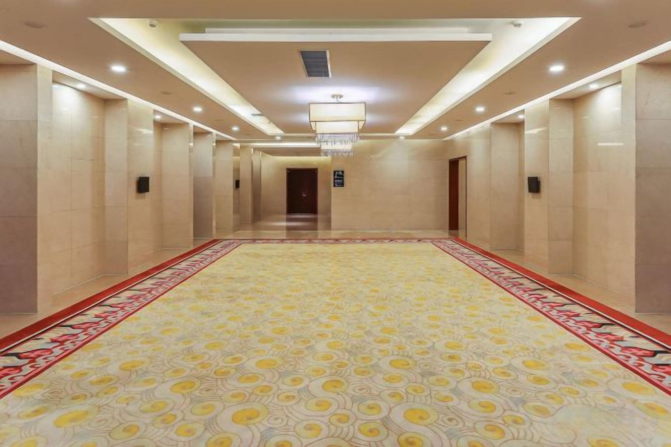A hotel corridor with a patterned carpet, doors on both sides, and a chandelier.