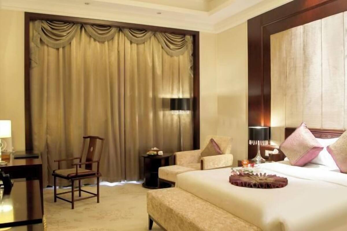 A hotel room with a large bed, a desk, a chair, and a window with curtains.