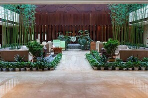 Un vestíbulo amplio con zona de estar central, plantas en macetas y un mostrador de recepción de madera.