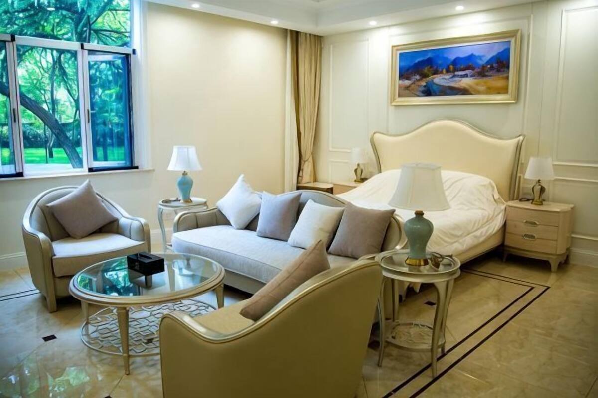 A hotel room with a bed, two chairs, a round coffee table, and a painting on the wall.