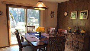 A dining area with a wooden table, chairs, and a chandelier. There is a sliding glass door leading to an outdoor area.