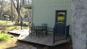 A wooden deck with a table and chairs, a small shed in the background, and a tree trunk to the right.