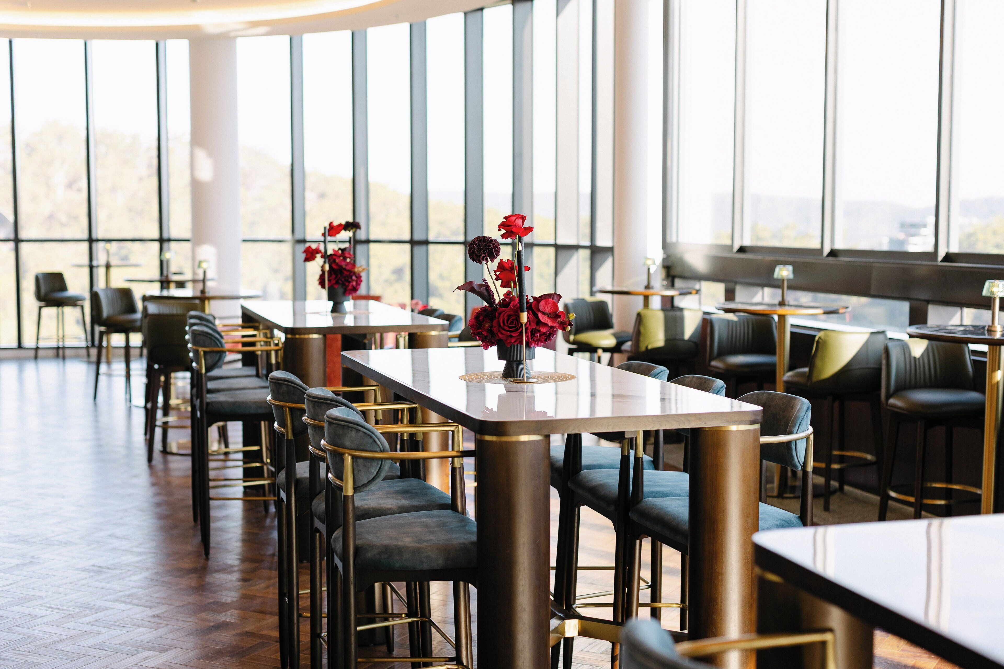 A restaurant with high tables and chairs, large windows, and a view of the outdoors.