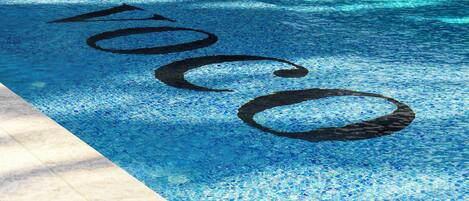 A swimming pool with a mosaic pattern and the word "POCO" written in the water.