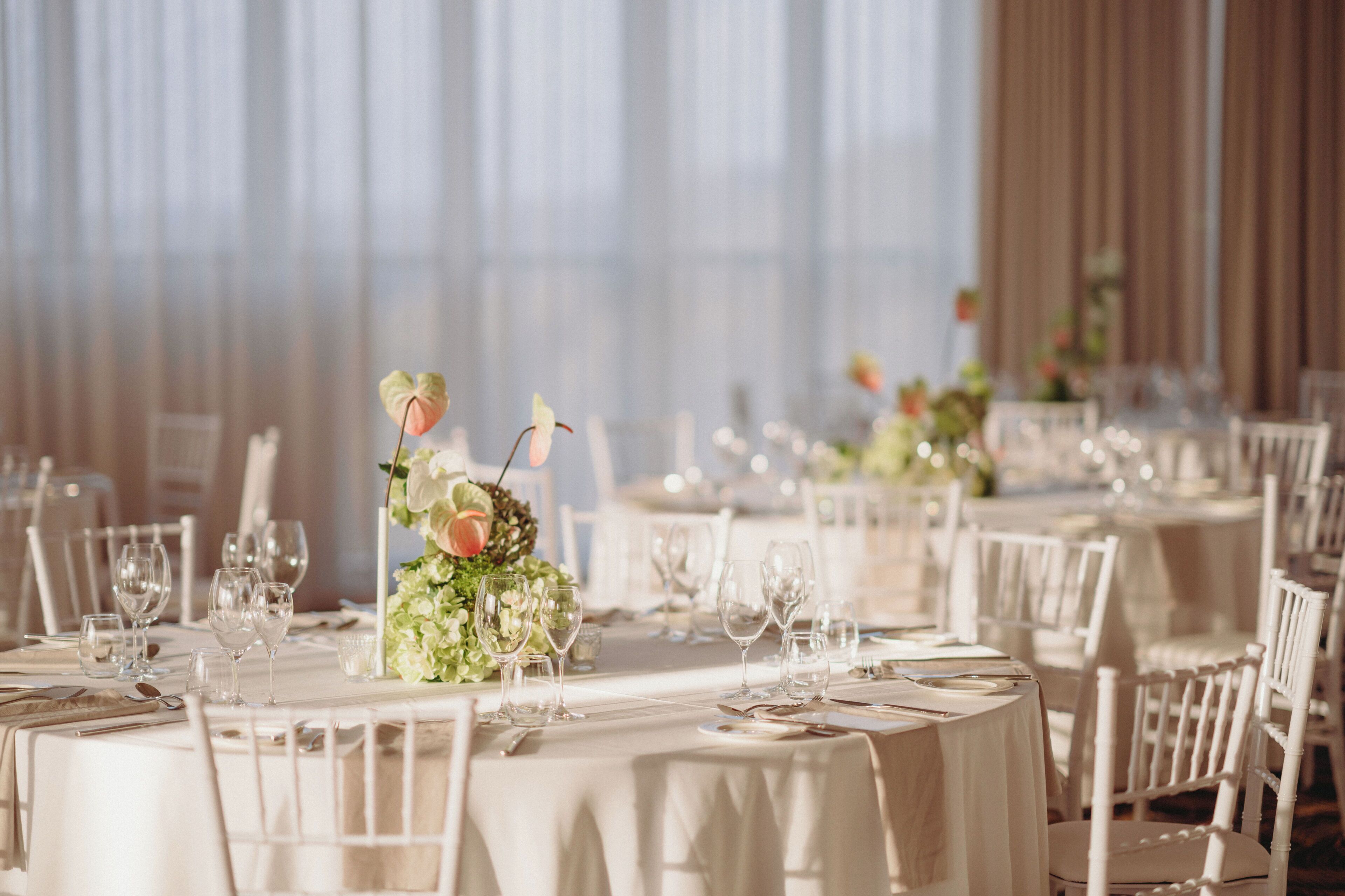 Un salón de banquetes con mesas redondas dispuestas para el servicio de comidas, cada una con manteles blancos y cristalería.