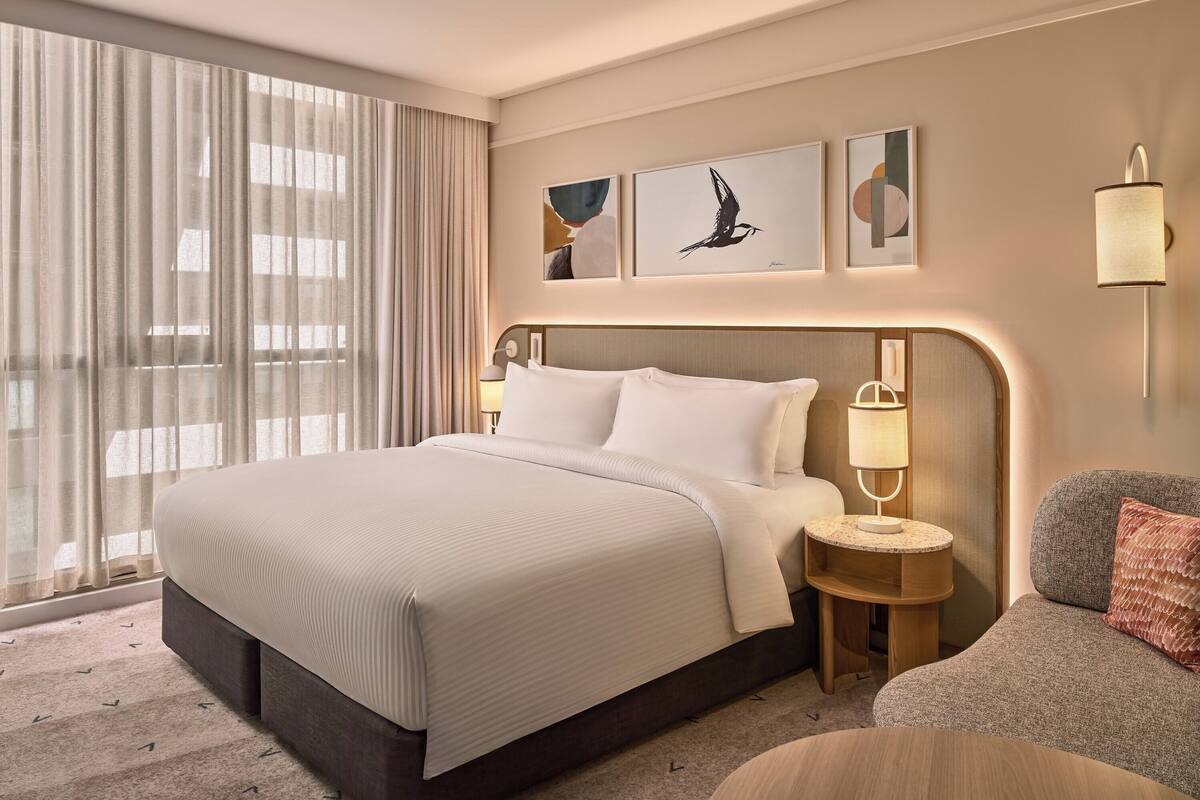 A hotel room with a large bed, a bedside table with a lamp, a sofa, and artwork on the wall.