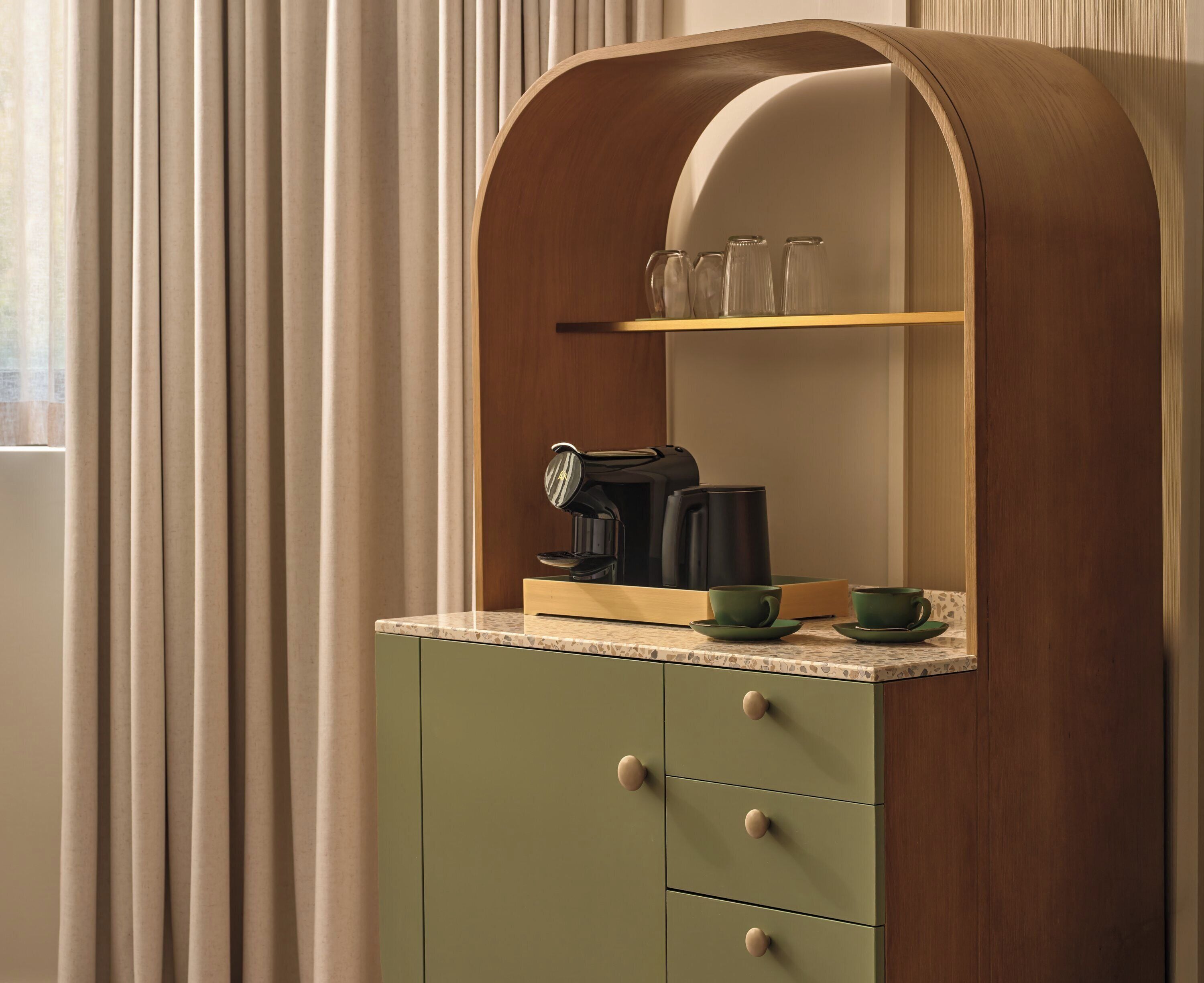 A kitchen with a wooden cabinet, a coffee maker, and a shelf with glassware.