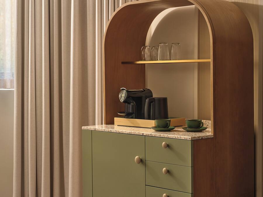 A kitchen with a wooden cabinet, a coffee maker, and a shelf with glassware.