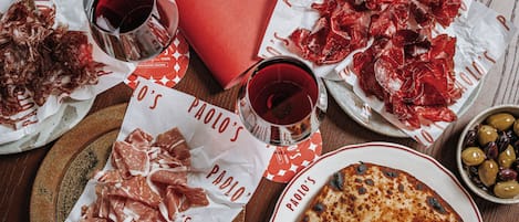 A table with various food items, including plates of cured meats, a pizza, and a bowl of olives.