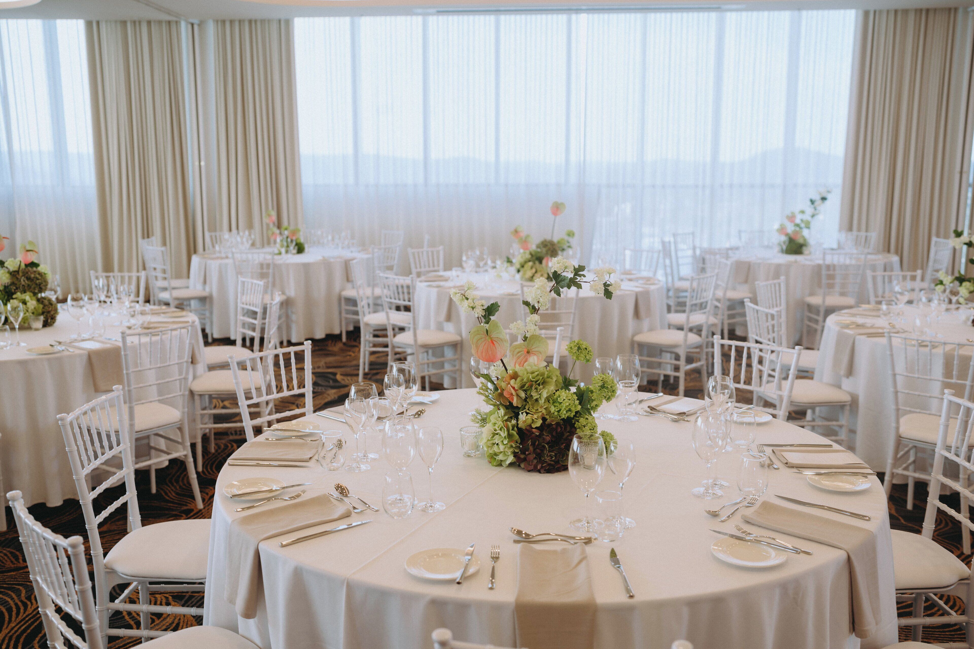 A banquet hall with round tables set for dining, white chairs, and floral centerpieces.
