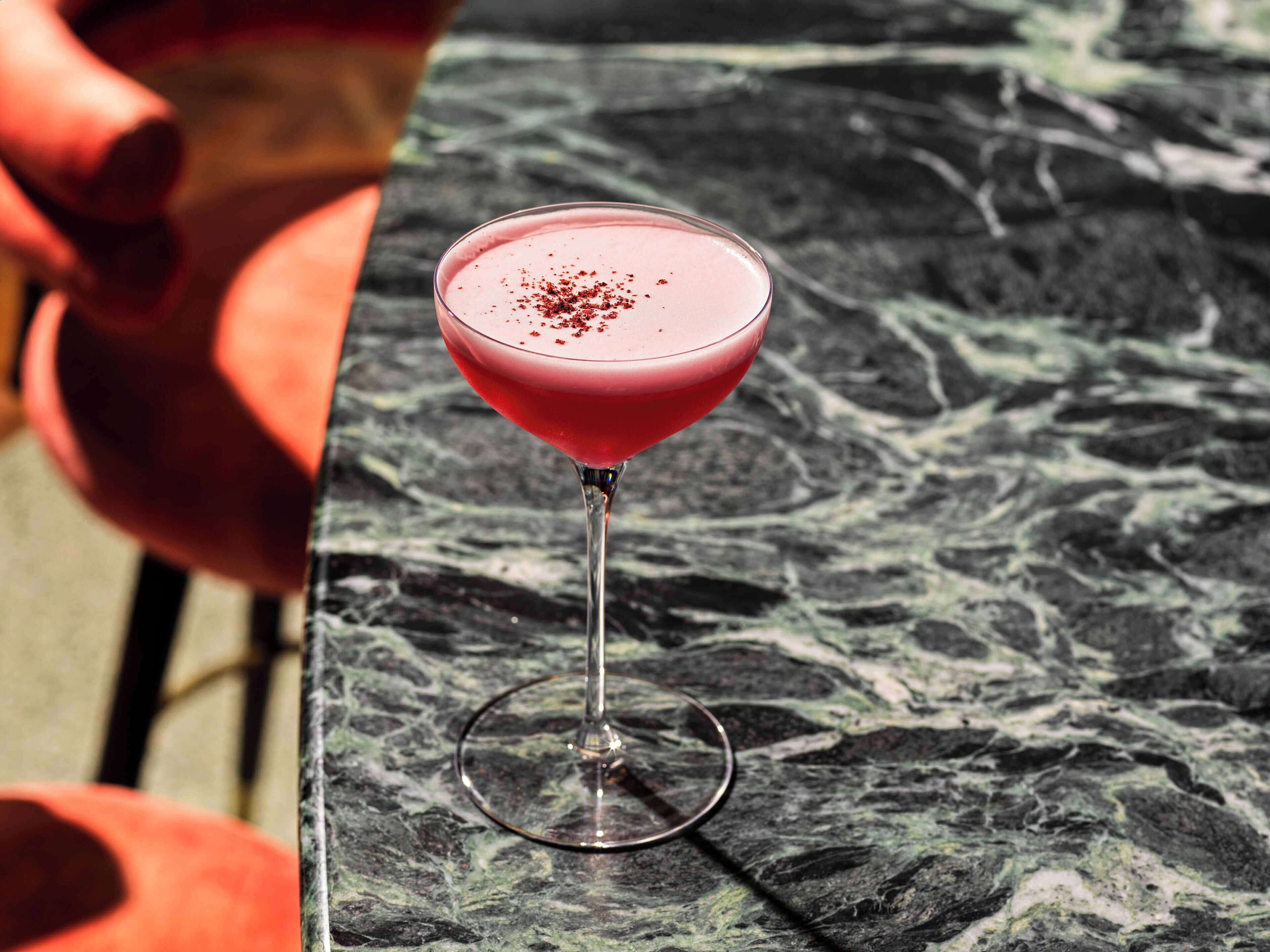 Una copa de martini con una bebida rosada sobre una mesa de mármol.