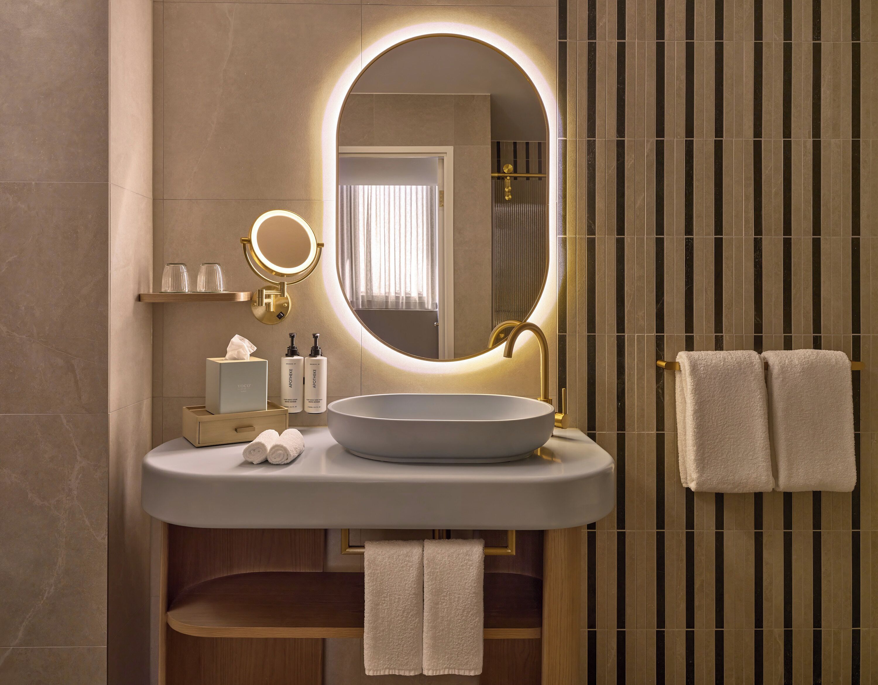Une salle de bain moderne avec un grand miroir ovale, un lavabo rond et deux serviettes suspendues à un porte-serviettes.