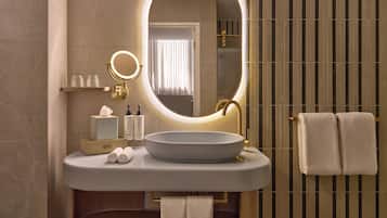 Une salle de bain moderne avec un grand miroir ovale, un lavabo rond et deux serviettes suspendues à un porte-serviettes.