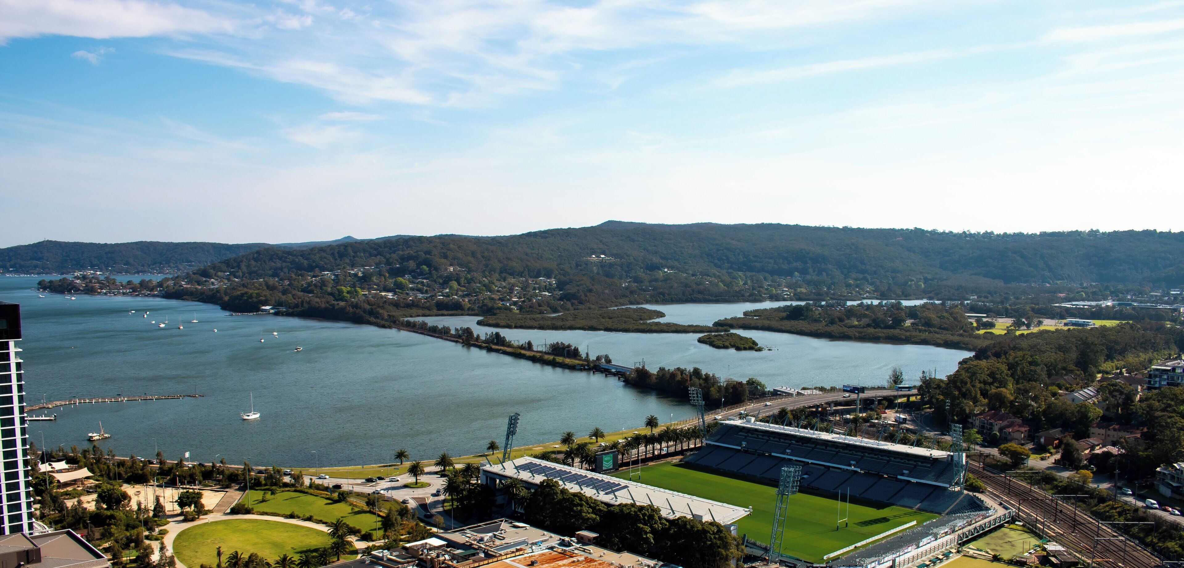 A stadium with a green field, surrounded by water and hills.